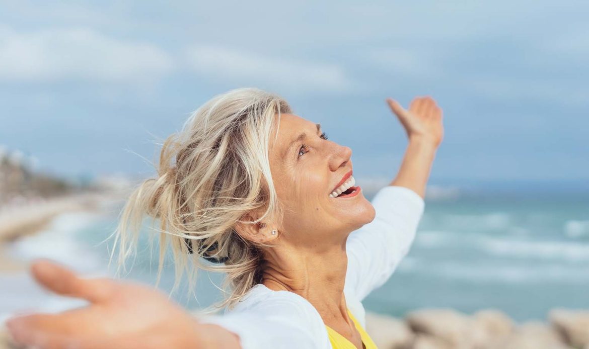 Woman standing by the ocean with arms outstretched, embodying the resilience and positivity of living with mental illness.