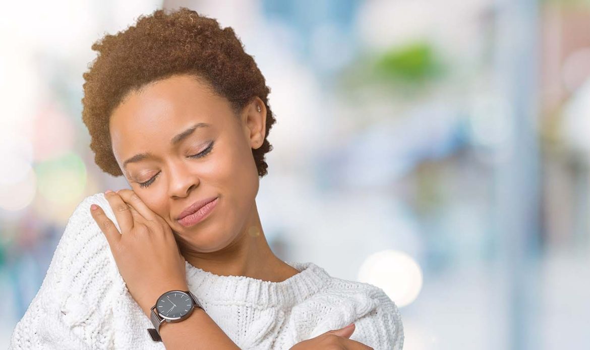 Woman hugging herself with a peaceful expression, symbolizing self-compassion and the practice of avoiding negative self-talk.