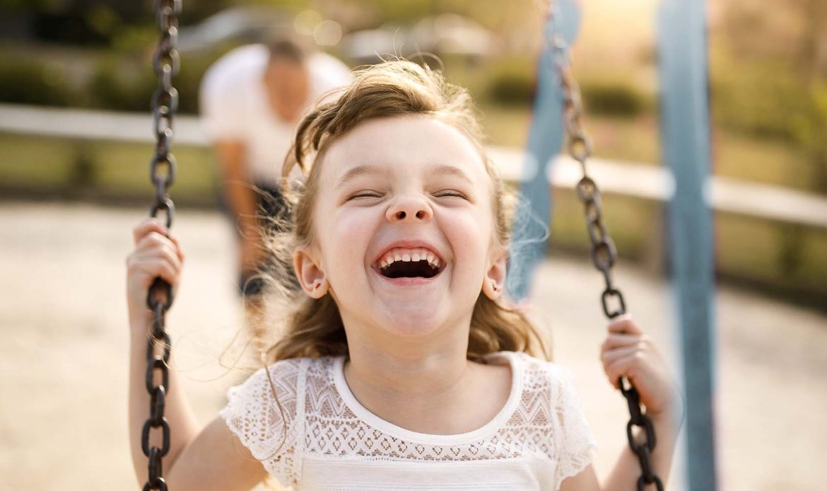 Young girl laughing joyfully on a swing, capturing a moment that reflects the essence of social-emotional development in children.