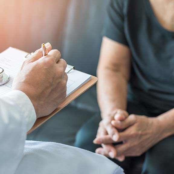 A healthcare professional writing notes on a clipboard while discussing with a patient, representing Schizophrenia symptoms and treatment.