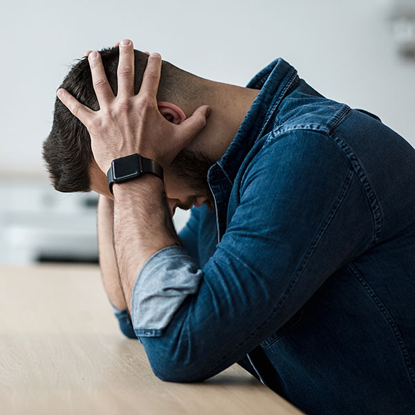 Person sitting at a table with hands on their head, showing signs of distress or anxiety, representing Unspecified Psychosis.