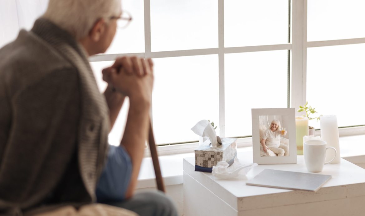 My deceased wife. Selective focus of a photo of a joyful nice elderly woman while being looked at be an unhappy senior man