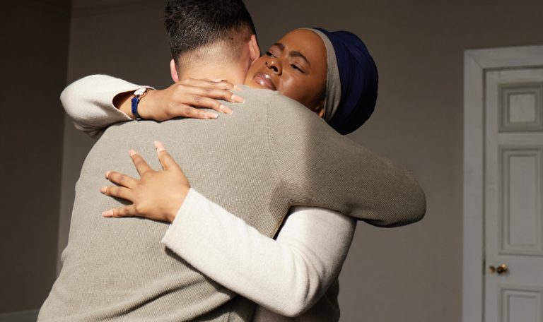 Hug, support and woman embrace a man for comfort, grief and care after bad news or problems in a home or house. Cancer, sad and depression by people hugging for empathy, love and hope together.