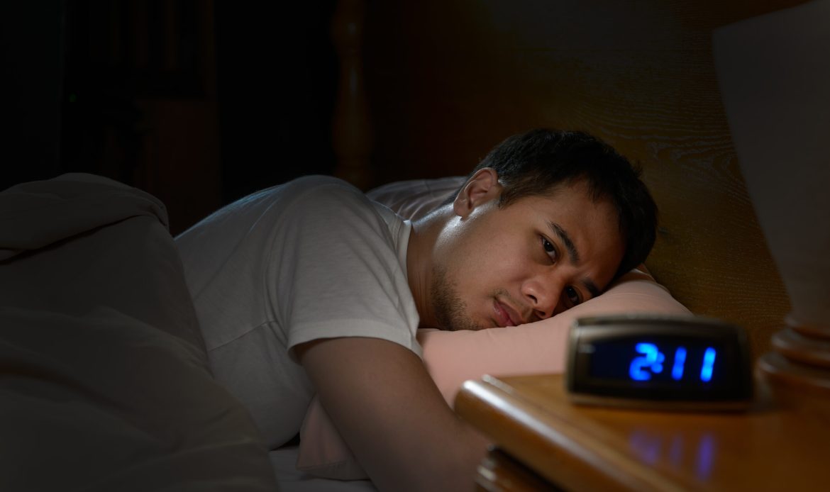 Depressed man suffering from insomnia lying in bed