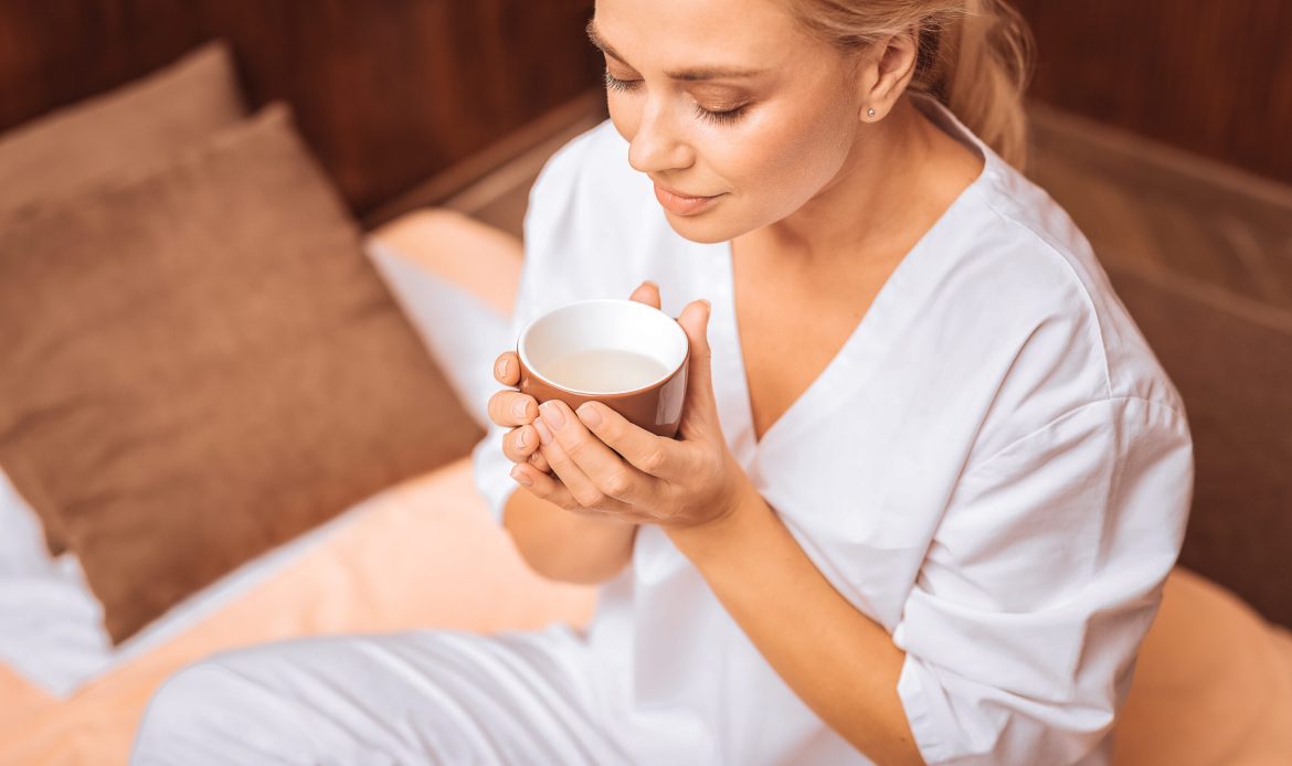 Pleasant drink. Delighted nice woman holding a cup of tea while preparing to drink it