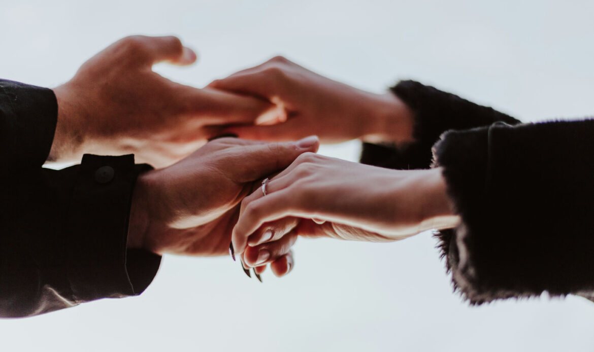 Close-up of two pairs of hands gently holding each other, conveying comfort and support in a time of sorrow.