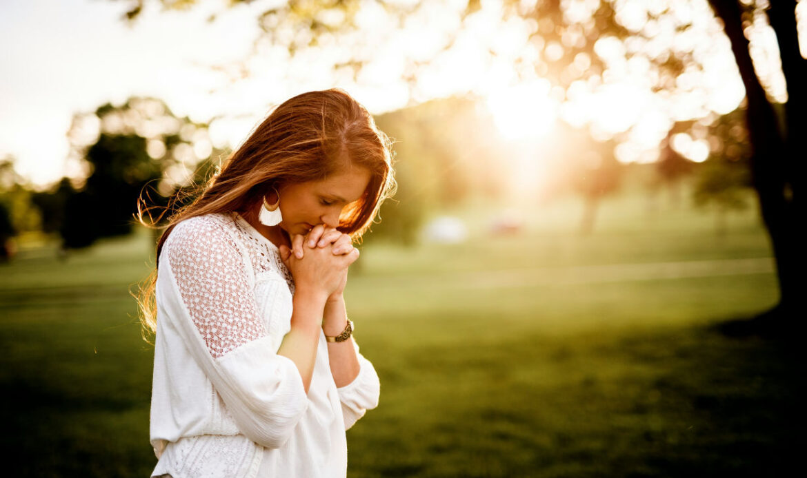 A woman standing in prayer in a peaceful setting, symbolizing hope and acceptance after losing a mother.