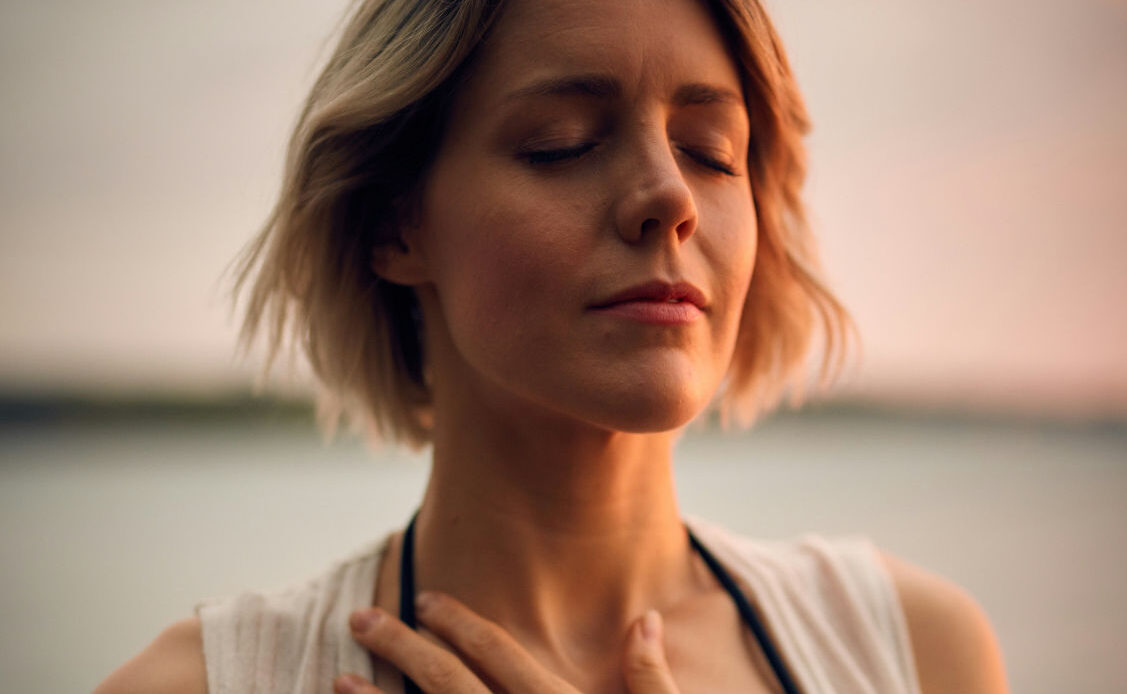 A person with eyes closed, hand on their chest, focusing on breathing and releasing grief.