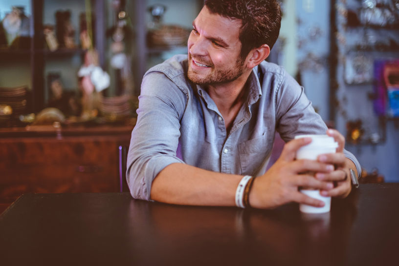 Man smiling while enjoying a coffee, showing that experiencing delayed grief doesn't mean you can't find moments of happiness.