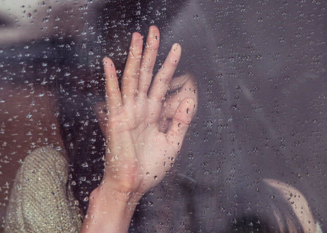 Grief vs Mourning shown with a sad woman touching a rain-covered window.