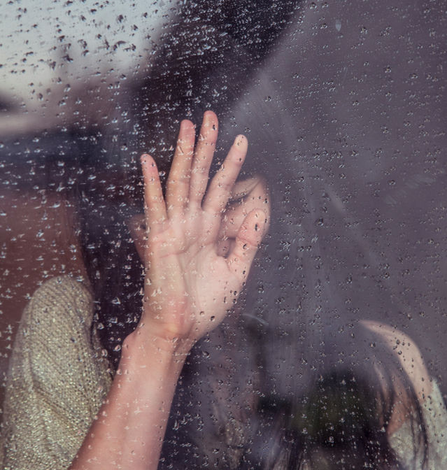 Grief vs Mourning shown with a sad woman touching a rain-covered window.