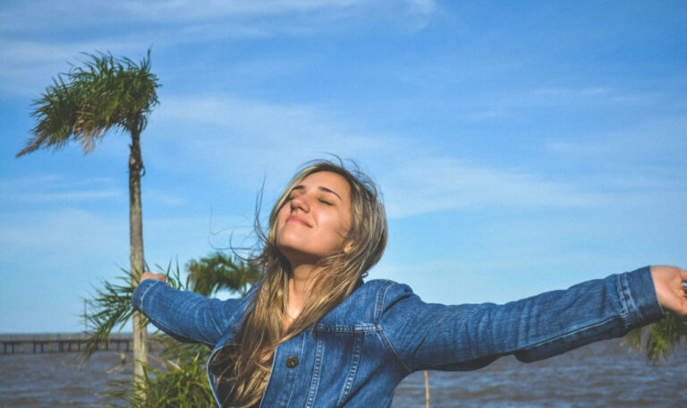 A person stands outdoors with arms outstretched and eyes closed, embodying the importance of understanding oneself for inner peace and fulfillment.