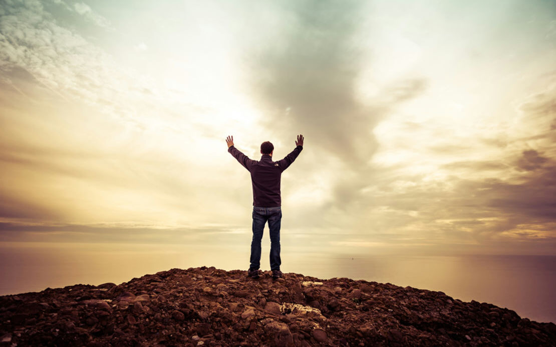 A person stands on a hilltop with arms raised toward the sky, symbolizing gaining a new perspective, reclaiming strength, and overcoming feelings of being a loser.