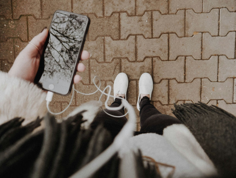 A person holds a phone with earphones plugged in while walking, symbolizing how listening to songs can provide comfort and support during the process of grief.