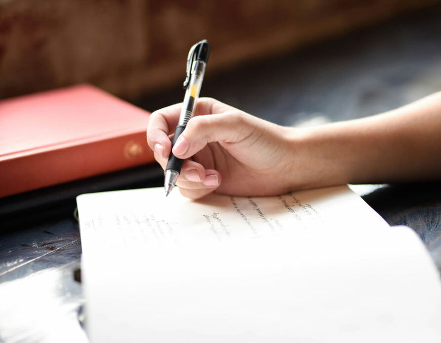 A hand holding a pen writes in a notebook, symbolizing the act of journaling as a way to process grief and let emotions flow freely onto paper.