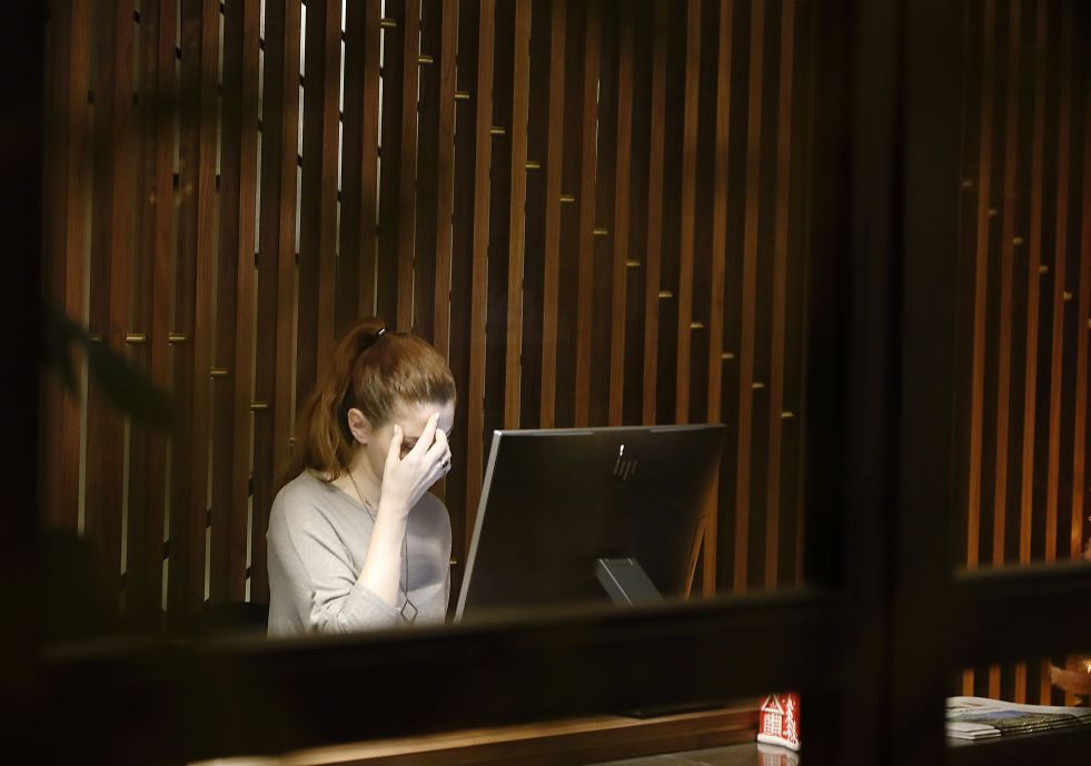 Person sitting at a desk holding their head, depicting masked grief.