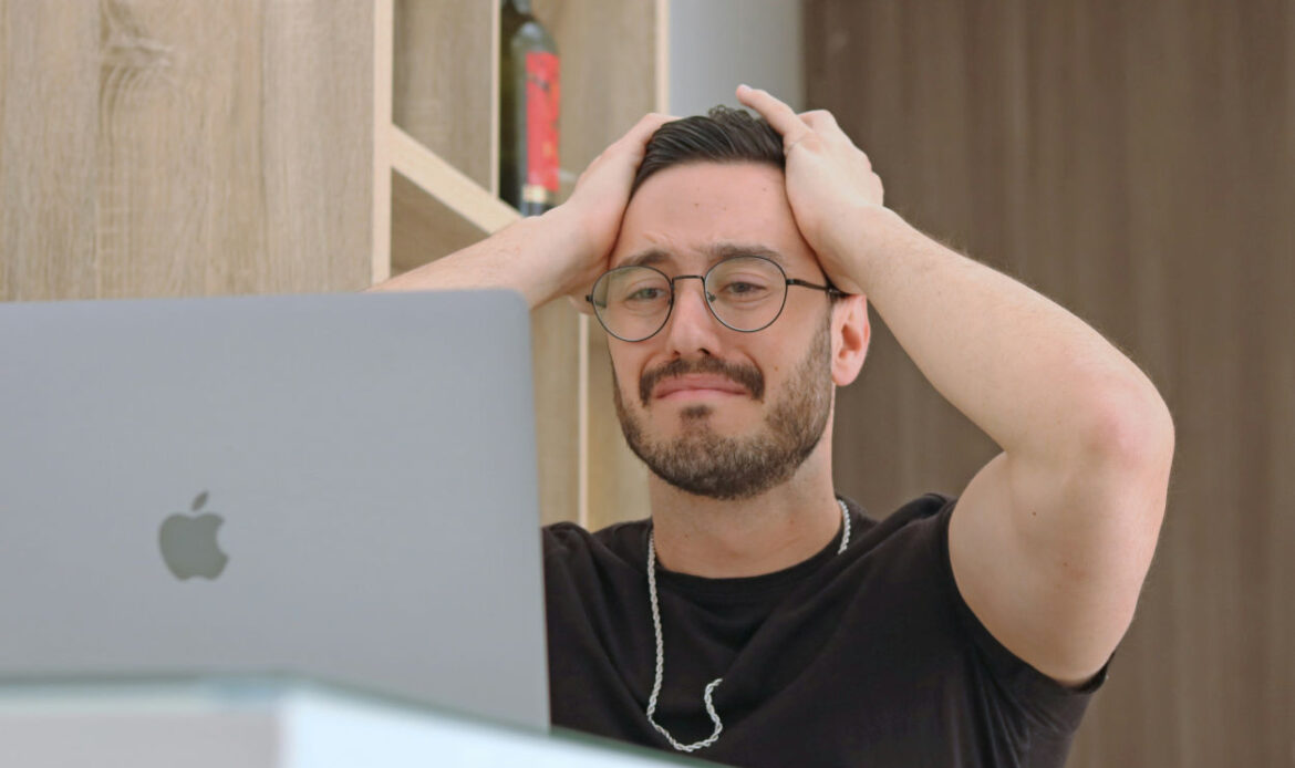 A man sits in front of a laptop, holding his head with a distressed expression, symbolizing the frustration and overwhelm that can come from feeling like a loser.