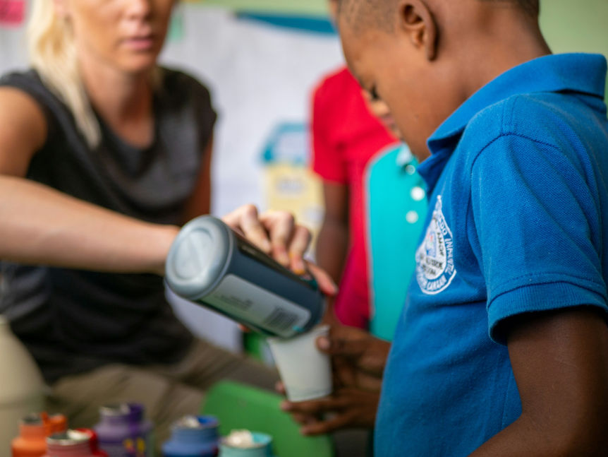 A child pours a drink with the help of an adult, representing paying it forward through acts of kindness as a way to find purpose and overcome feelings of being a burden.