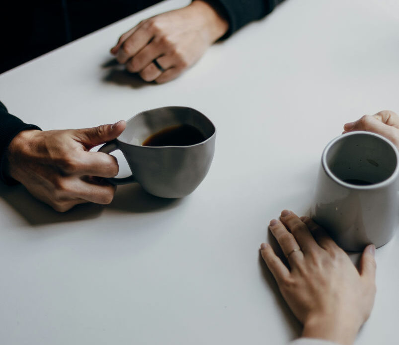 Two people sit at a table holding mugs, symbolizing connection, conversation, and the role of relationships in self-healing.