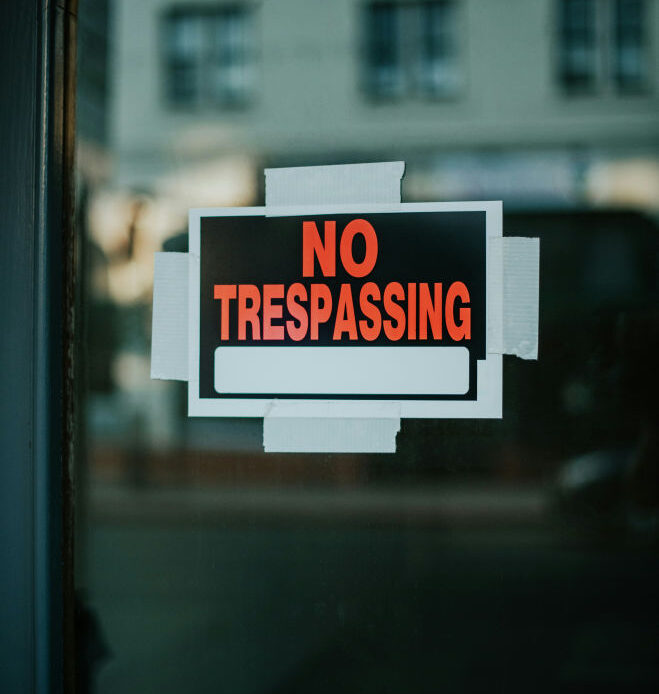  A "No Trespassing" sign taped to a glass door represents the concept of setting limits and taking steps to strengthen boundaries.