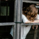 A woman leans out of a broken window with her head down, symbolizing isolation, overwhelm, and the weight of feeling like a burden.