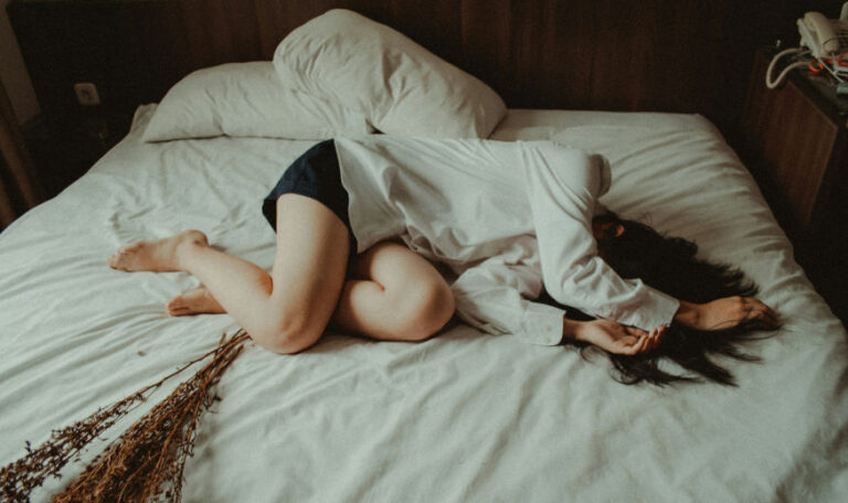 Person lying curled up on a bed, reflecting inhibited grief.