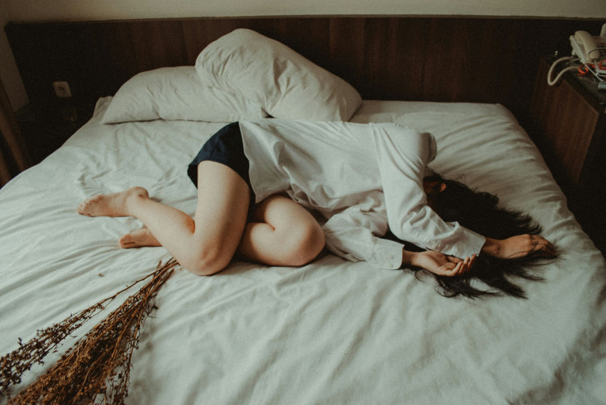 Person lying curled up on a bed, reflecting inhibited grief.