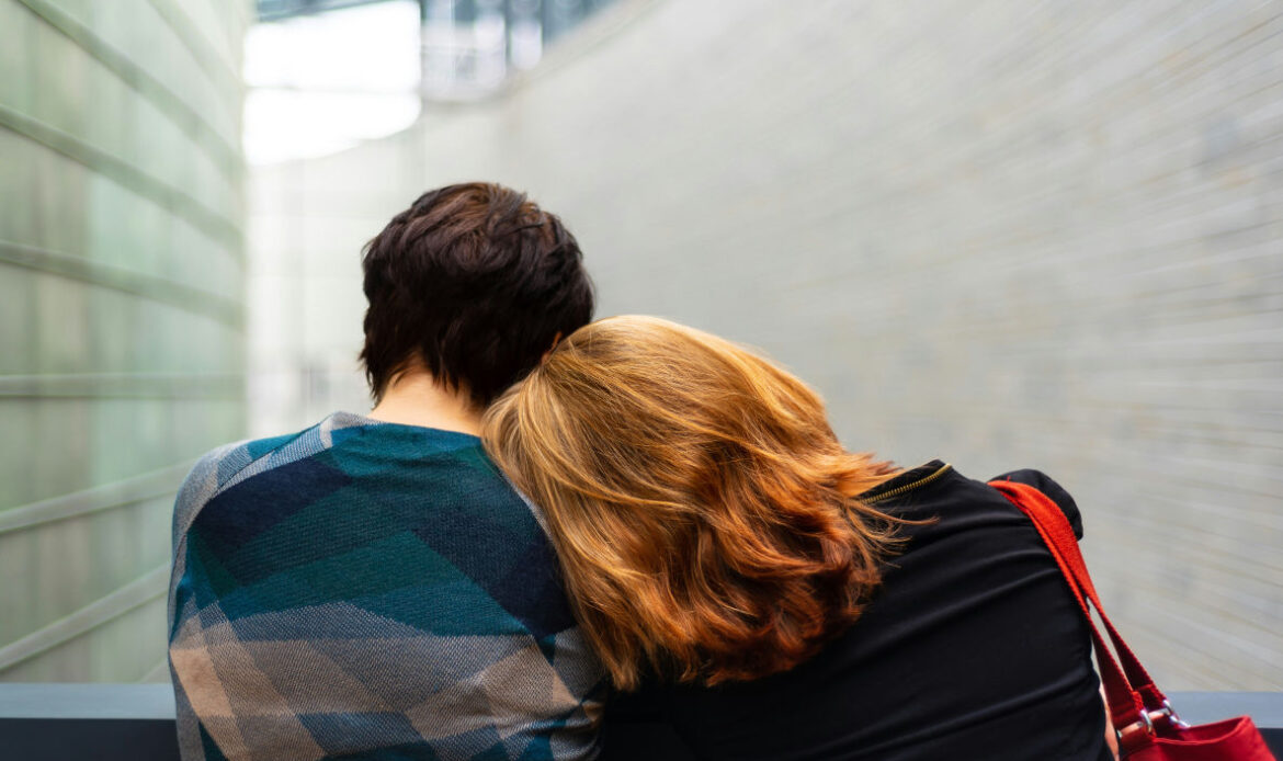 Two people sitting closely, with one person leaning their head on the other's shoulder, representing comfort and support while grieving on a one-year death anniversary.