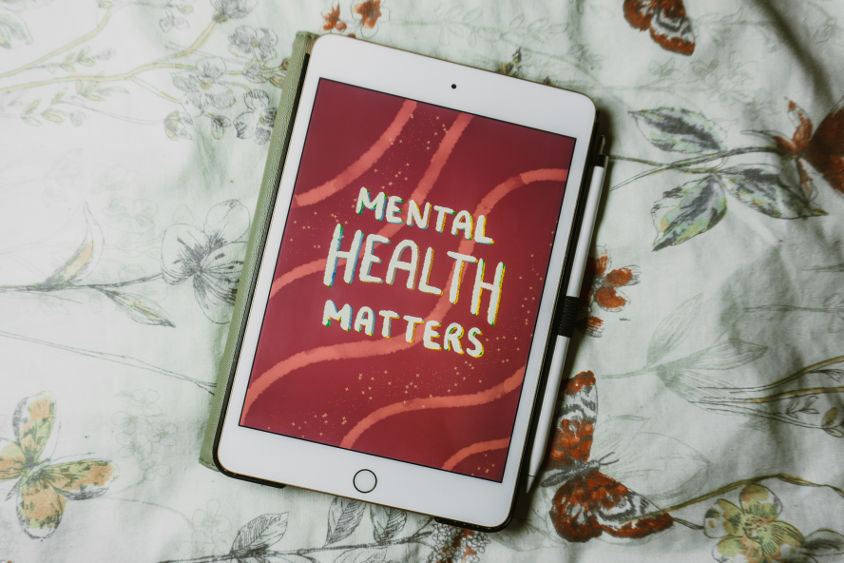 A tablet displays the words "Mental Health Matters" on a red background, representing the importance of setting and achieving mental health goals.