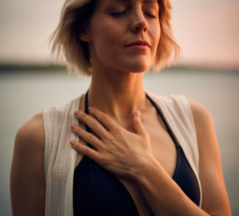 A woman with her eyes closed places her hand on her chest, embodying calmness and introspection as she begins to start the healing process.