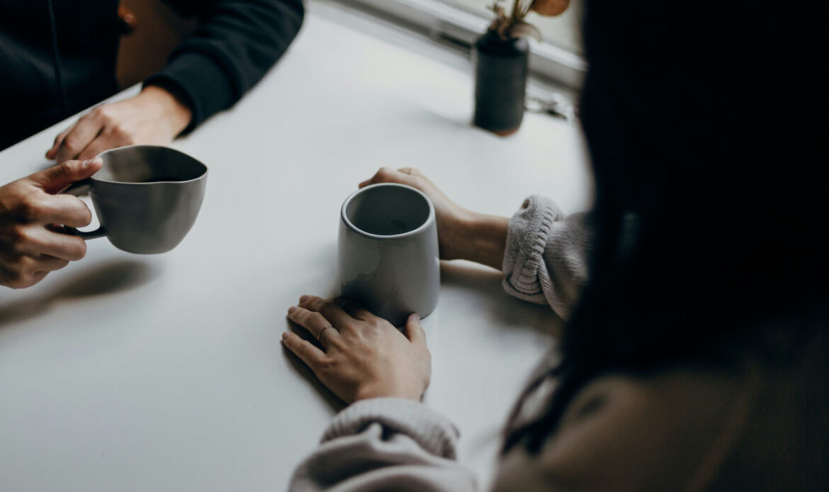 Two people sit together at a table with mugs in hand, symbolizing the importance of a support system to provide connection and help stop feelings of being a loser.