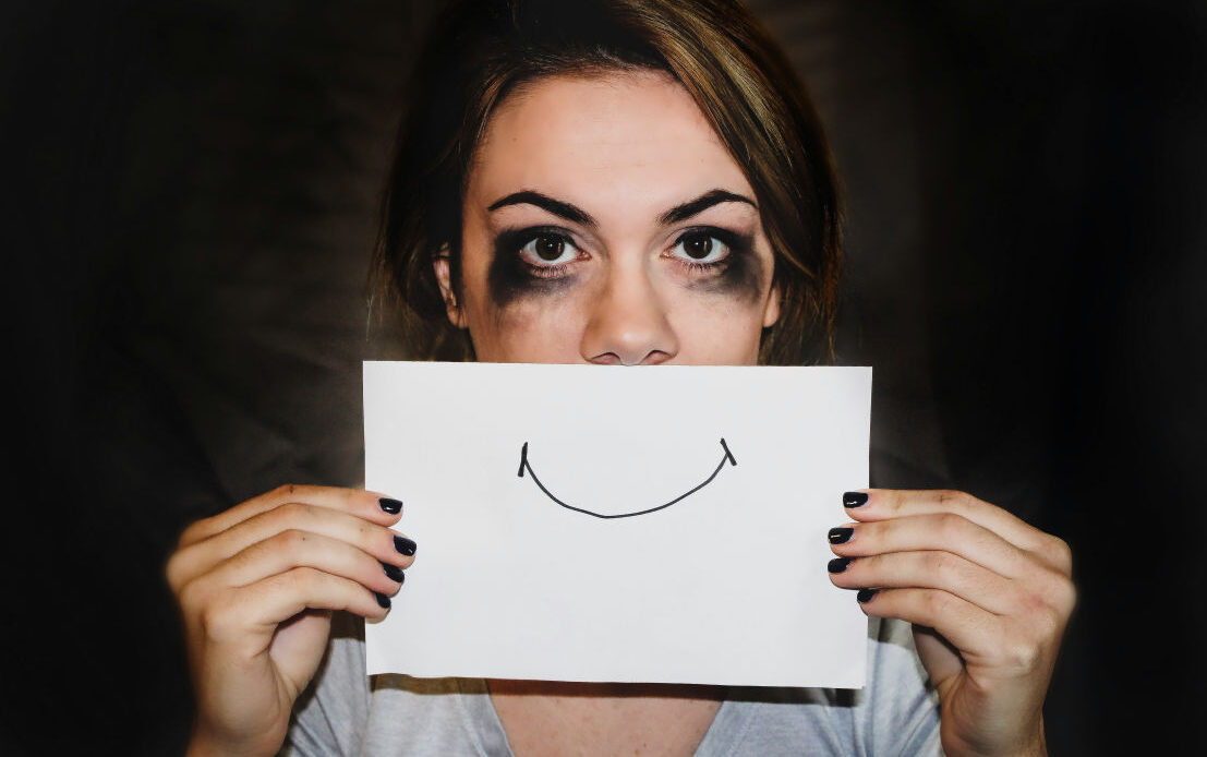 Person holding a paper with a drawn smile over their face, conveying inhibited grief.