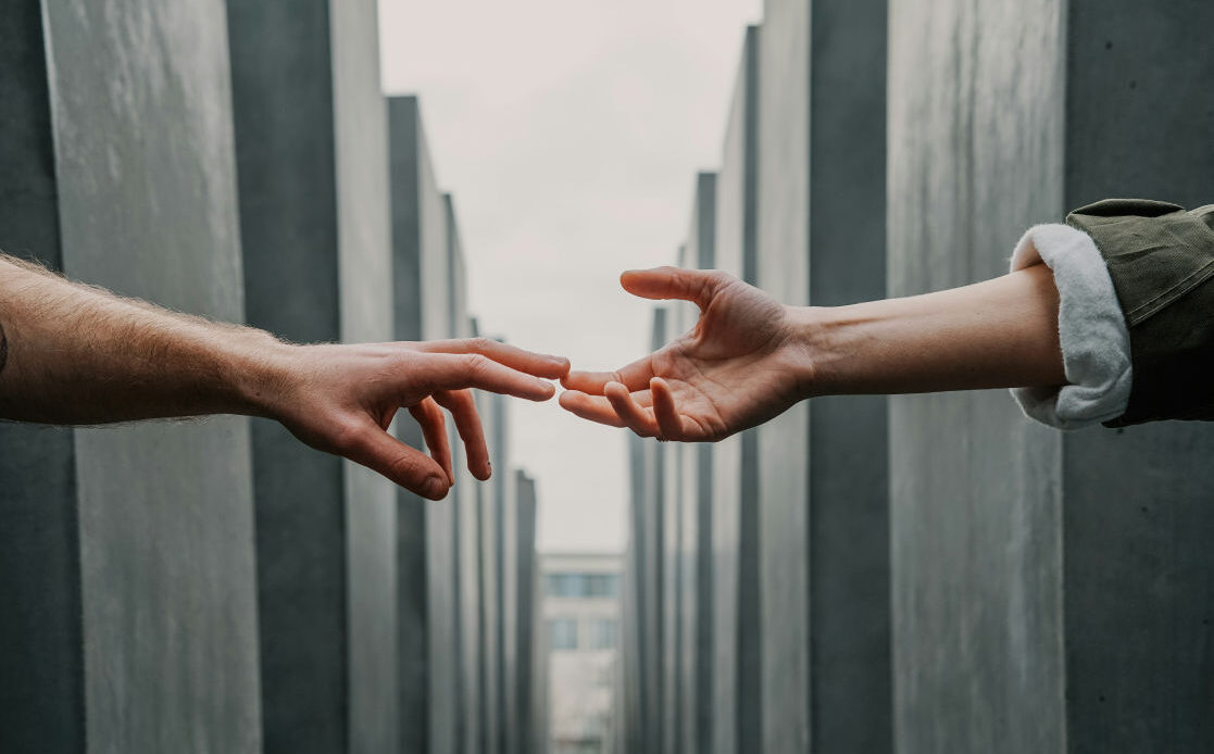 A woman’s hand reaches out towards another hand, symbolizing longing, grief, and the emotional connection to a husband she has lost.