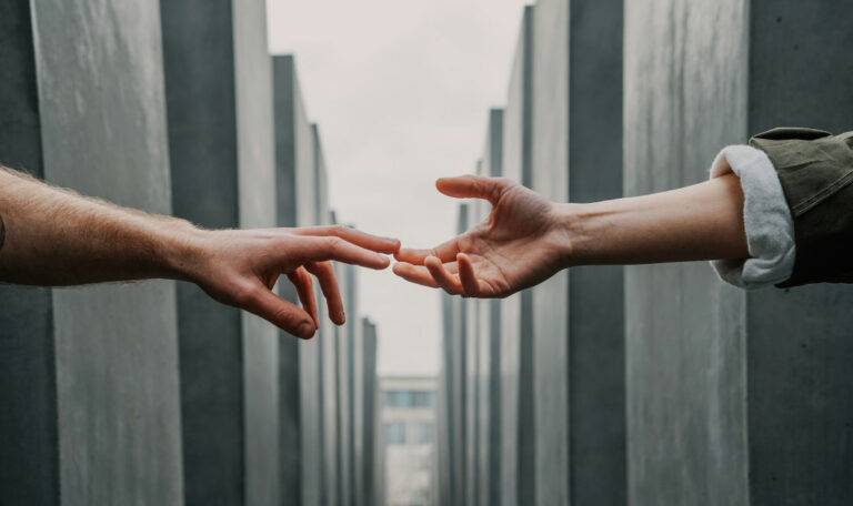 A woman’s hand reaches out towards another hand, symbolizing longing, grief, and the emotional connection to a husband she has lost.