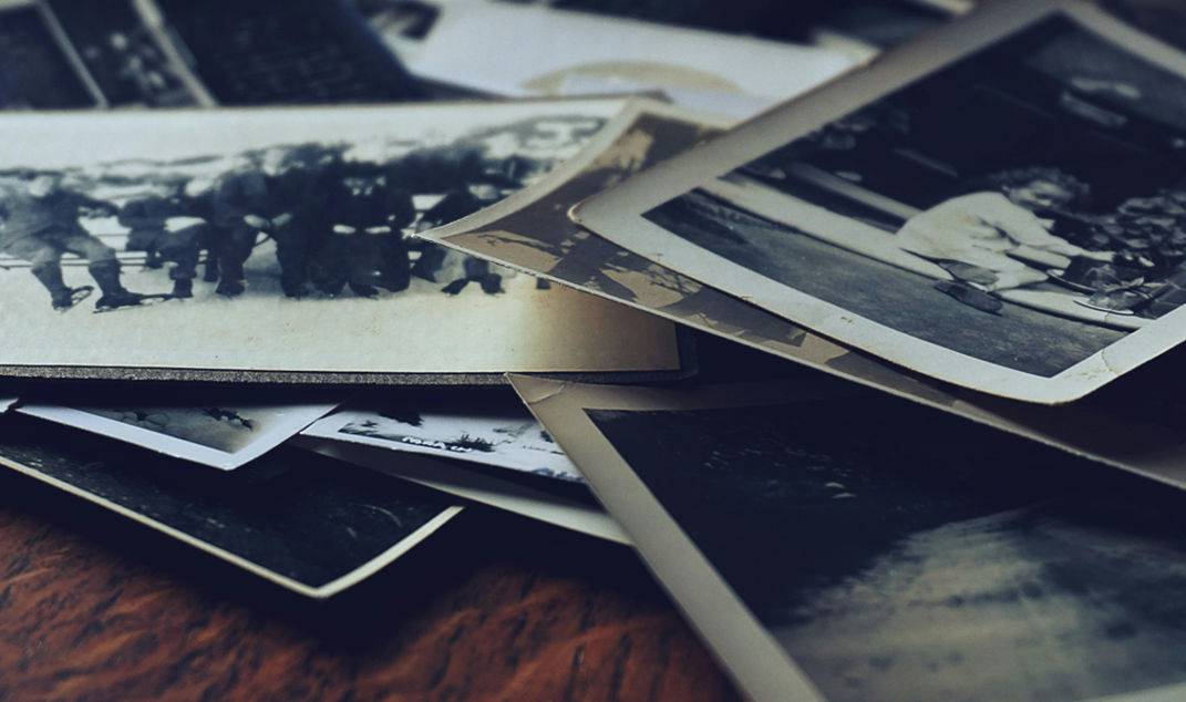 A stack of old black-and-white photographs scattered on a wooden surface, symbolizing memories and the process of confronting unresolved grief and allowing oneself to feel the pain of loss.