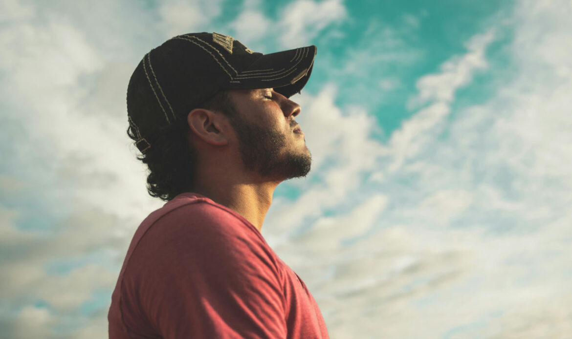 A man wearing a cap and red shirt stands with his eyes closed, facing the sky, embodying a moment of peace and self-reflection, symbolizing the practice of using healing affirmations for personal growth.