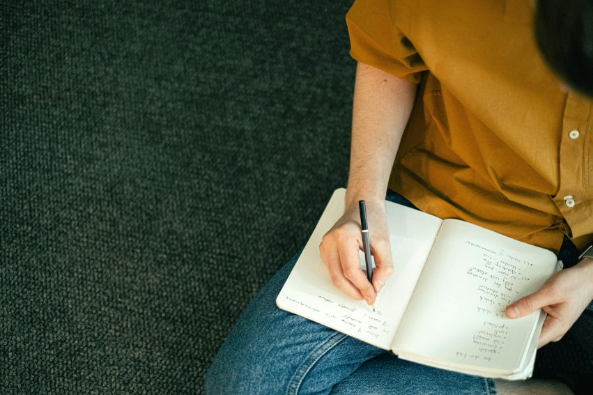 Person sitting on the floor, writing goals or plans in a notebook, symbolizing steps to start over with strength and clarity.