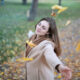 A woman standing in a park with her arms outstretched, eyes closed, and surrounded by falling autumn leaves, symbolizing peace and healing affirmations.