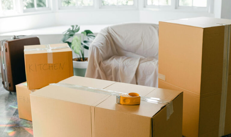 A room filled with packed cardboard boxes, a covered chair, and a suitcase, symbolizing a fresh start or moving to a new phase in life.