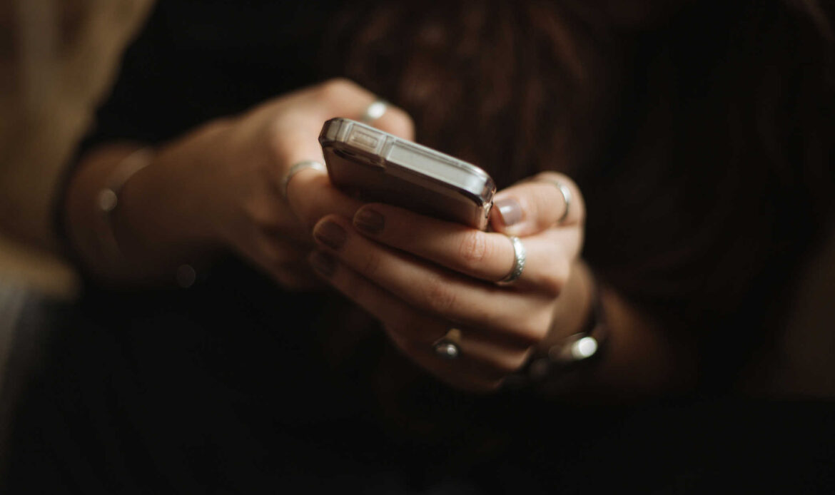 Person holding a smartphone with both hands, possibly reaching out for help or encouragement as part of overcoming adversity.