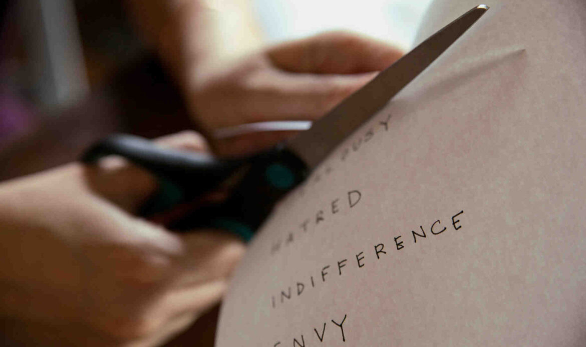 Person cutting a paper with the words 'hatred,' 'indifference,' and 'envy' written on it, symbolizing release of negative emotions.