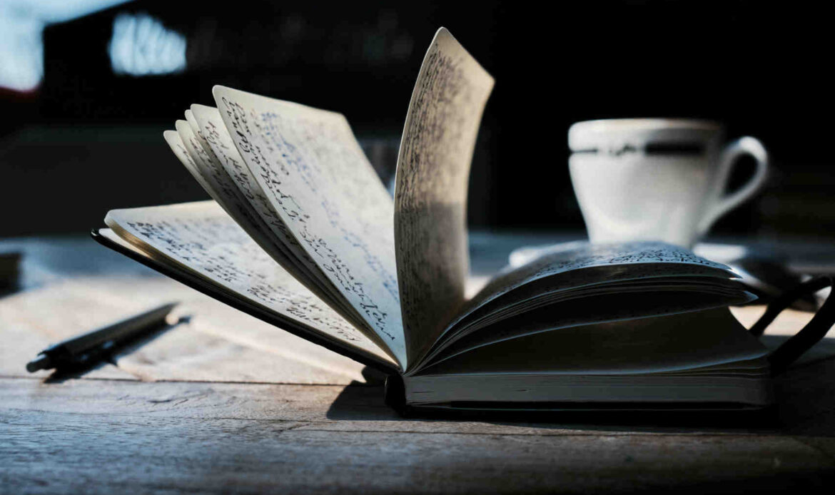 Open journal with handwritten notes on a wooden table beside a cup of coffee, capturing the act of reflective writing.