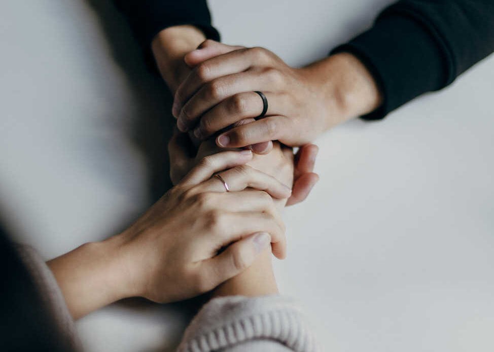 Two people holding hands across a table, symbolizing connection, care, and emotional support.