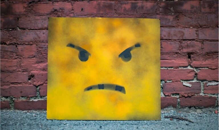 Spray-painted canvas showing an angry face leaning against a brick wall, symbolizing dealing with disappointment and frustration.