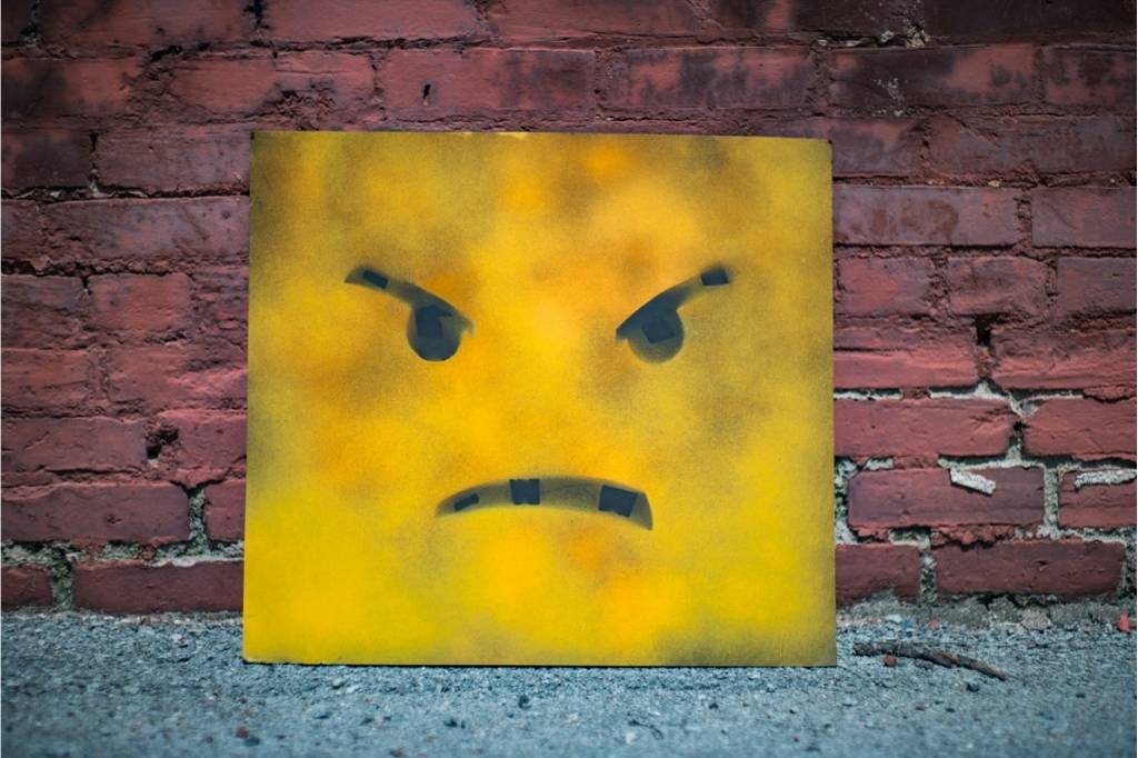 Spray-painted canvas showing an angry face leaning against a brick wall, symbolizing dealing with disappointment and frustration.