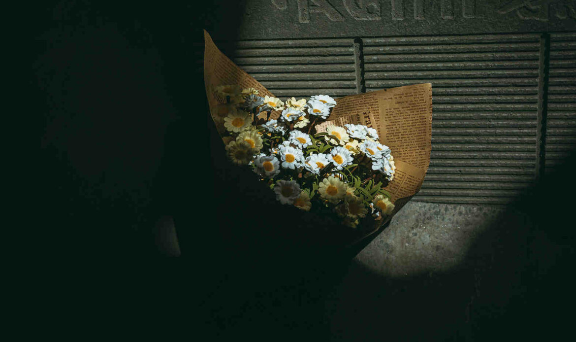 Bouquet of daisies wrapped in newspaper resting on the ground, symbolizing quiet sympathy and how to comfort someone who lost a loved one.