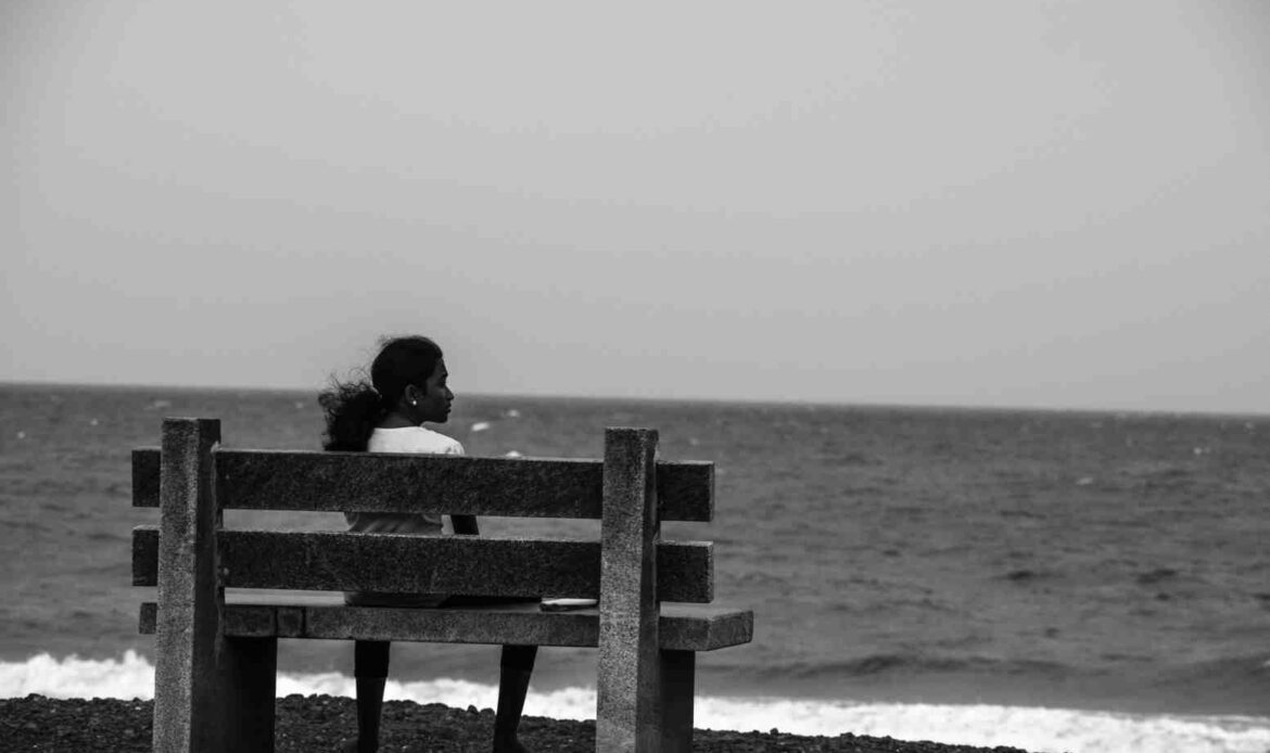 Person sitting alone on a bench by the ocean, capturing the quiet presence of comforting someone who lost a loved one.