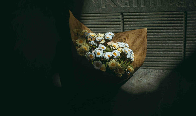 Bouquet of daisies wrapped in newspaper resting on the ground, symbolizing quiet sympathy and how to comfort someone who lost a loved one.