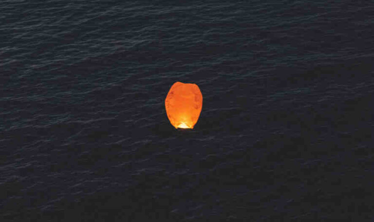 Single floating lantern glowing over dark water at night, symbolizing release.