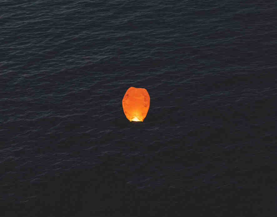 Single floating lantern glowing over dark water at night, symbolizing release.